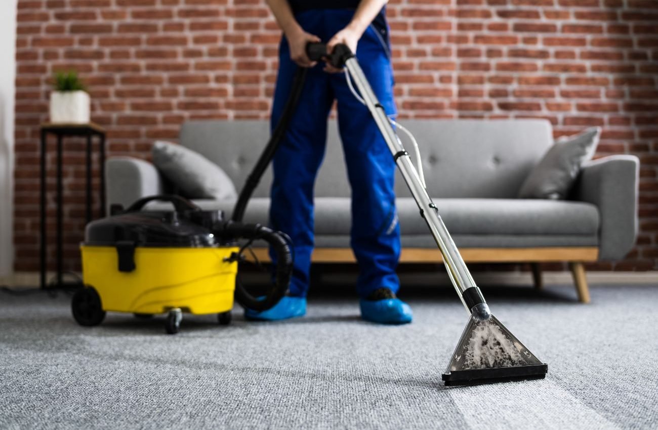 A man in blue overalls uses a vacuum to clean a carpet, highlighting a rug cleaning service in Los Angeles, CA.